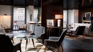 Ein modernes Wohnzimmer mit einem Glastisch, grauen Sesseln, einem beigen Sofa und einer dunkelholzverkleideten Wand.