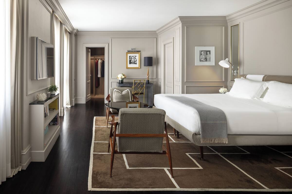 Habitación de hotel con una cama grande, un escritorio con silla, una mesita con lámpara y un armario.