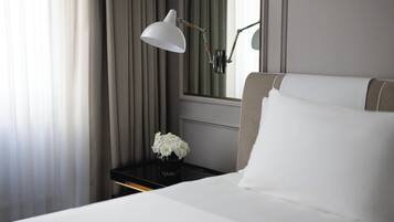 Une chambre d’hôtel avec un lit, une table de chevet, une lampe de bureau, un vase de fleurs et un grand miroir.