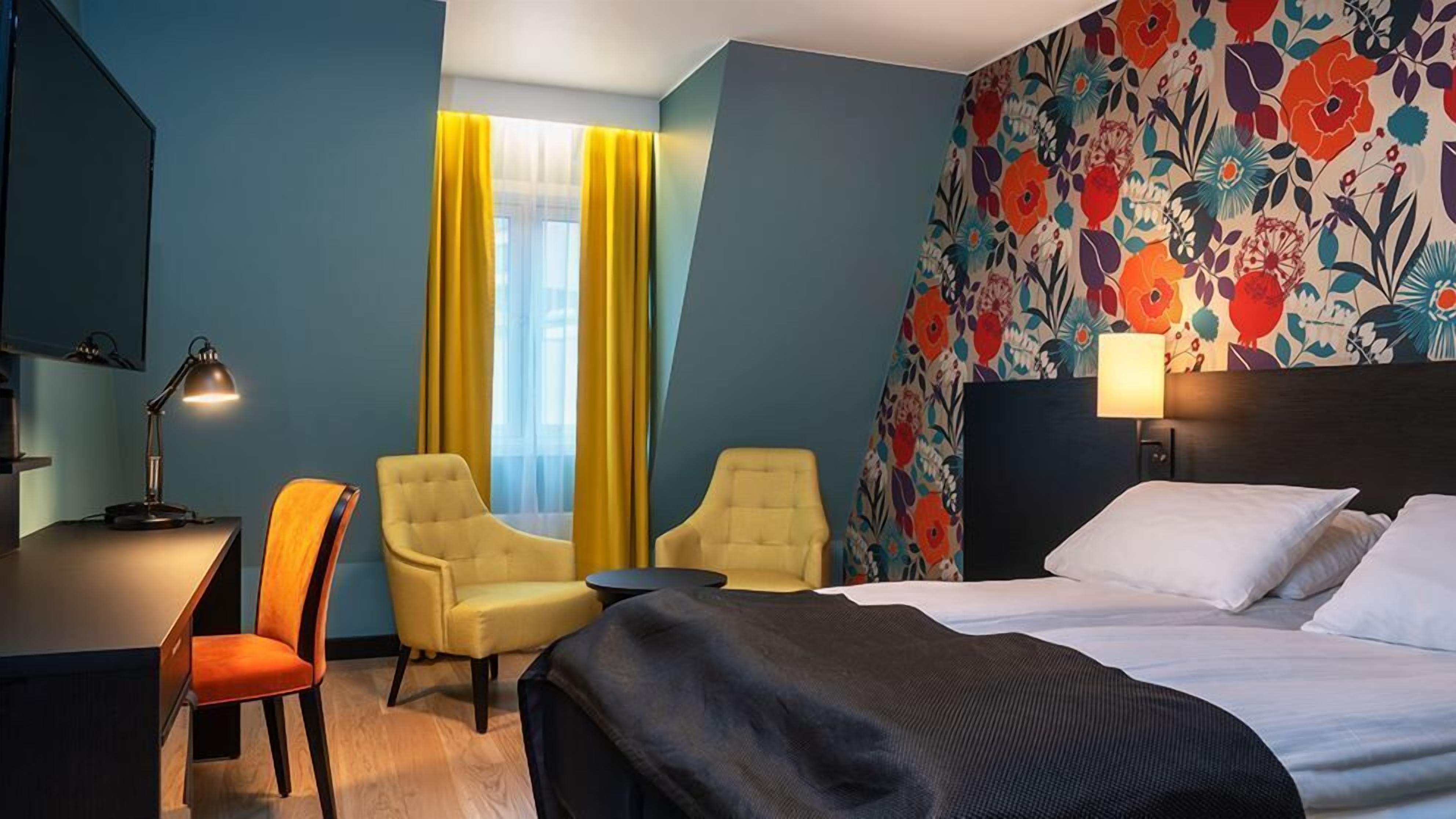 A hotel room with a bed, two armchairs, a desk, and a lamp.