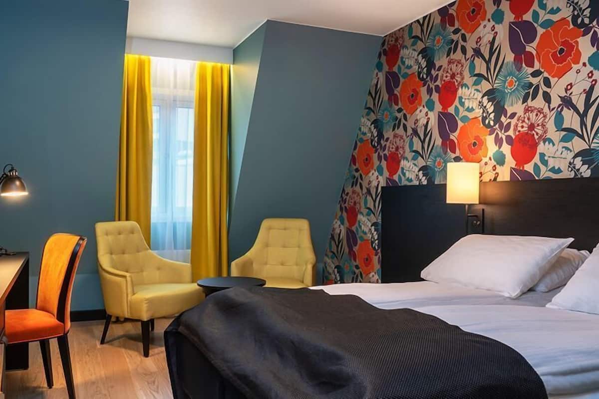 A hotel room with a bed, two armchairs, a desk, and a lamp.