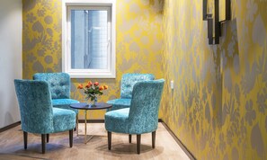 A room with two turquoise chairs, a small table with a vase of flowers, and a window with blinds. - Thon Hotel Harstad (Harstad)