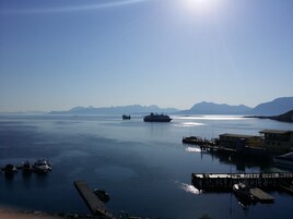 Un puerto tranquilo con barcos amarrados, un muelle y montañas lejanas bajo un cielo despejado.
