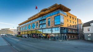 A modern hotel with a prominent glass facade, multiple balconies, and a flag on top. - Thon Hotel Harstad (Harstad)