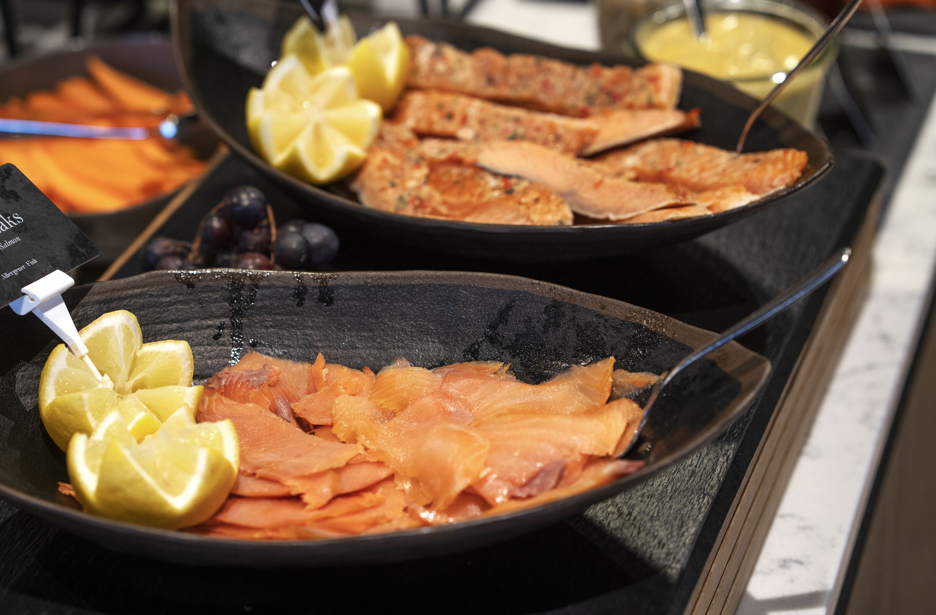 Un bufé con diferentes opciones de comida, incluyendo salmón, rodajas de limón y un tazón de sopa.