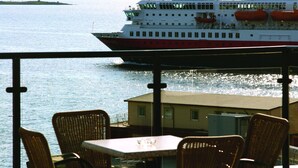 A dining area with wicker chairs and a table, overlooking a calm body of water with a cruise ship and mountains in the background. - Thon Hotel Harstad (Harstad)