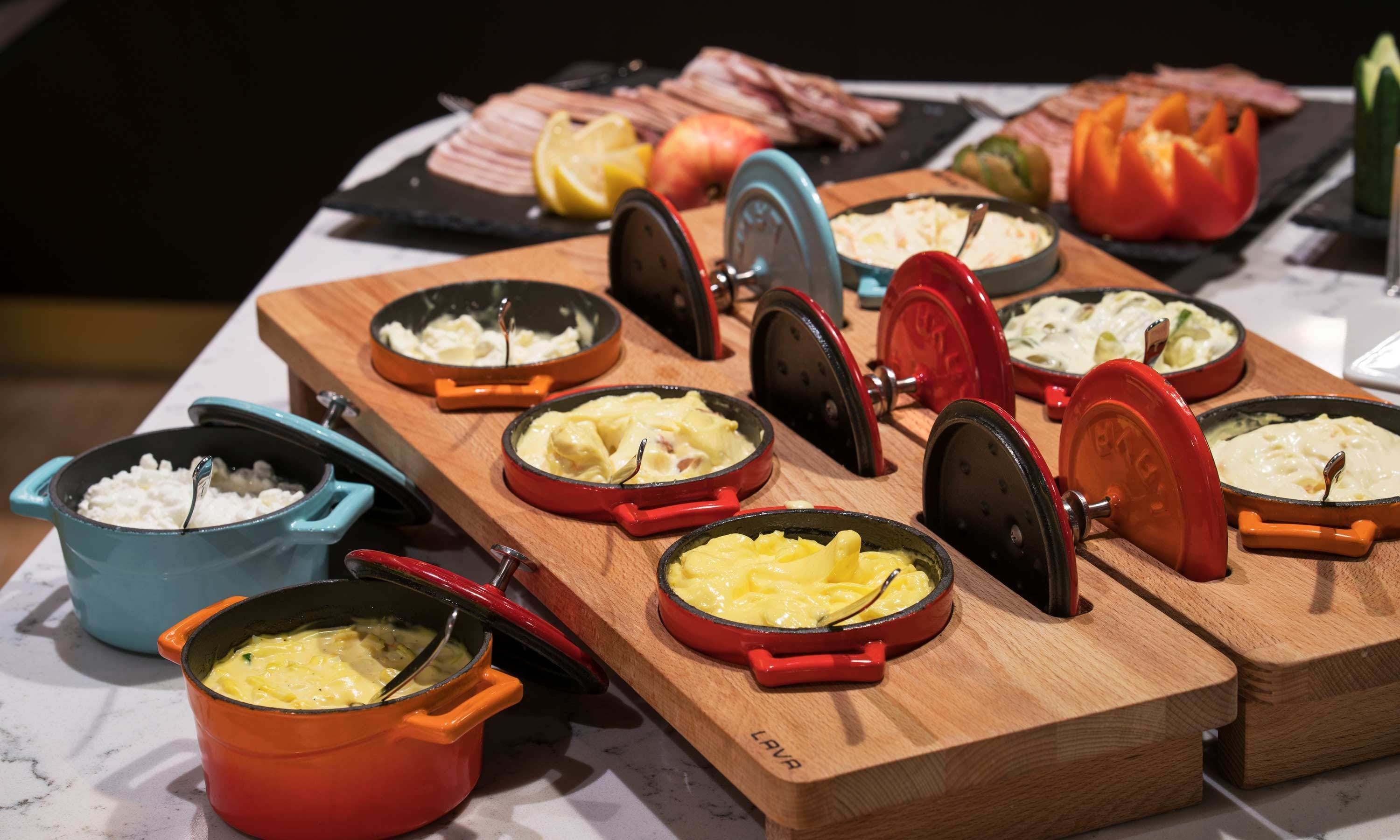 A buffet table with various dishes in cast iron skillets, including cheese and potato dishes, and a selection of meats and vegetables.