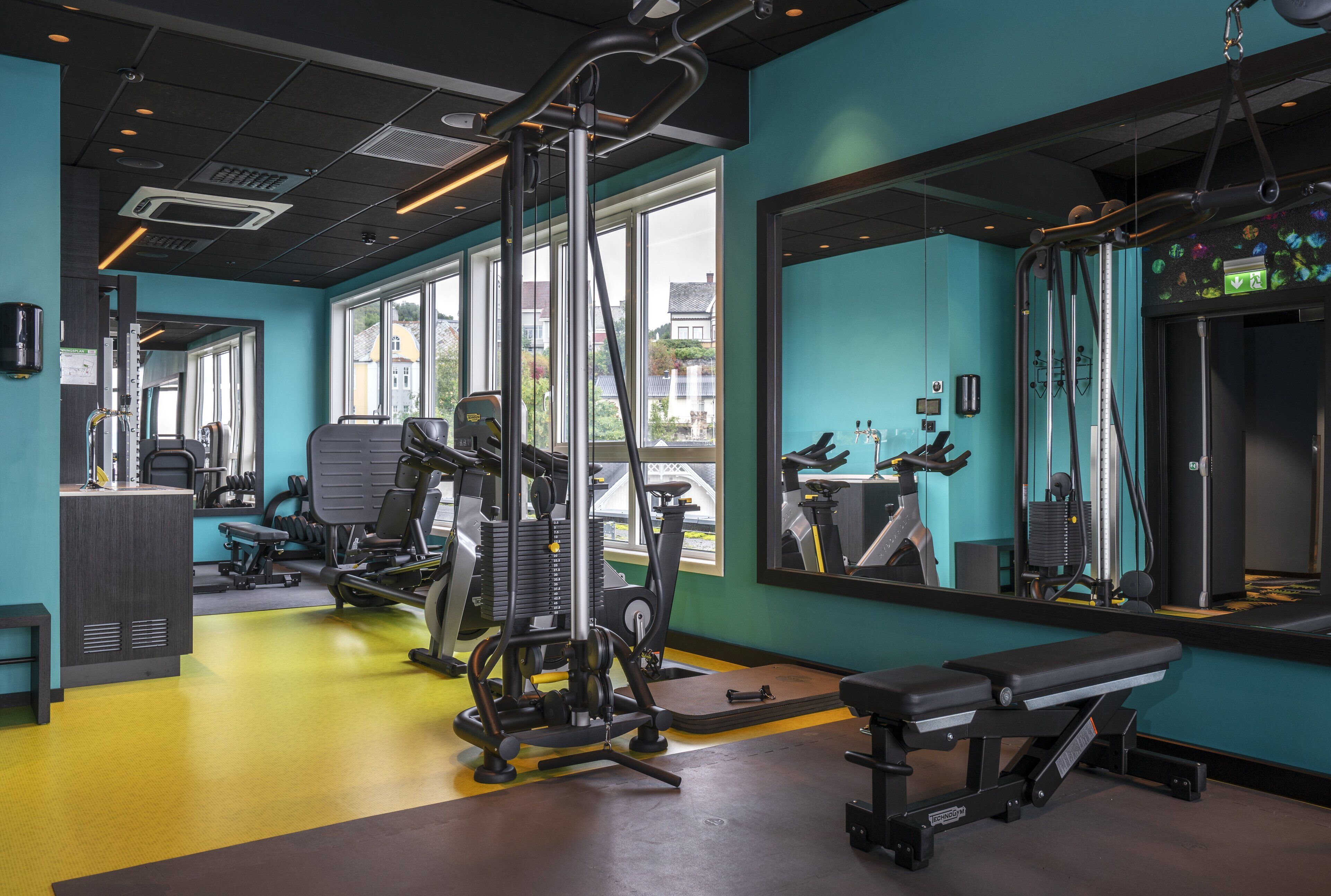 A gym with exercise equipment, large windows, and a bench.