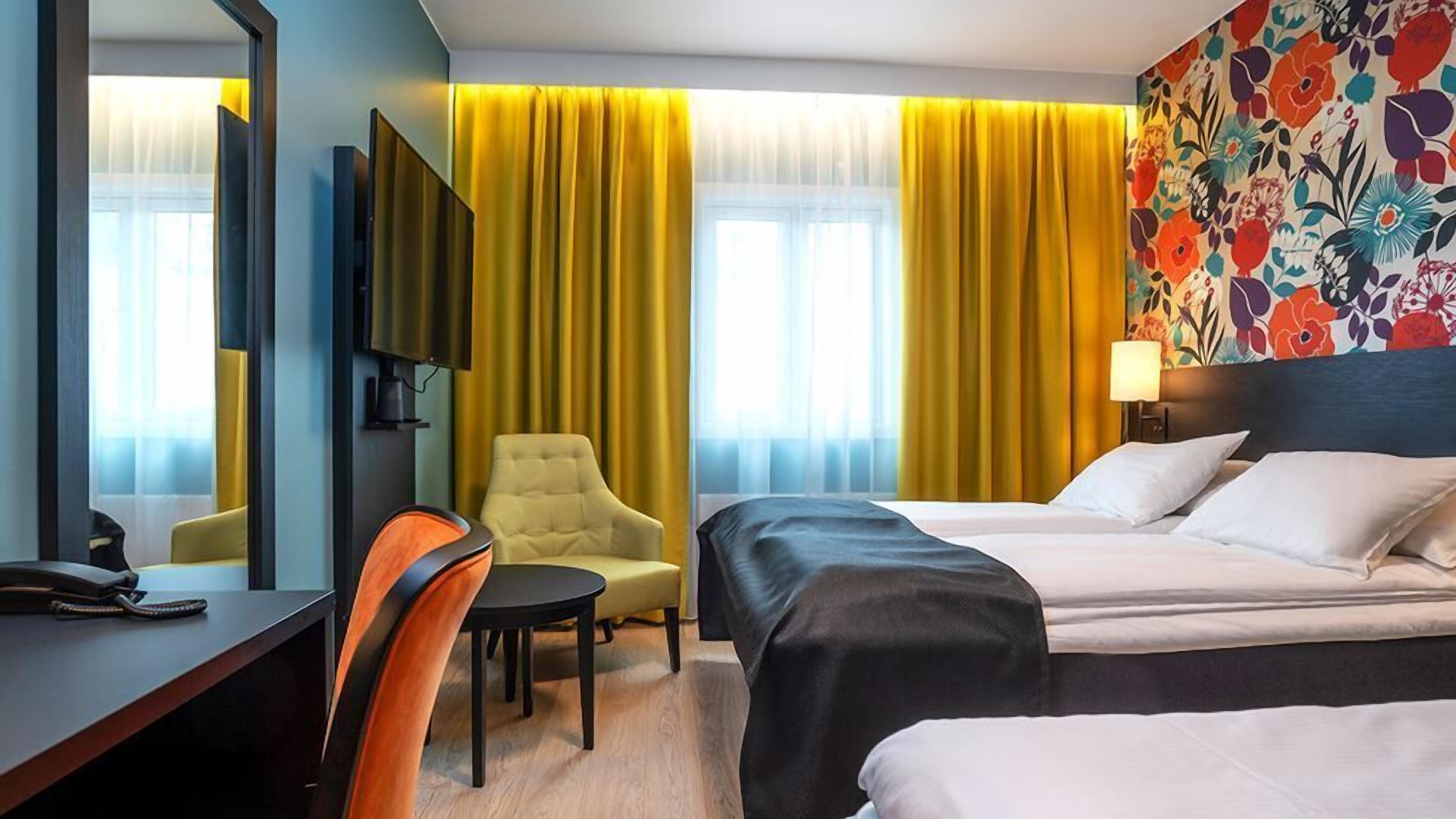 A hotel room with a bed, a desk, a chair, a TV, and a window with curtains.