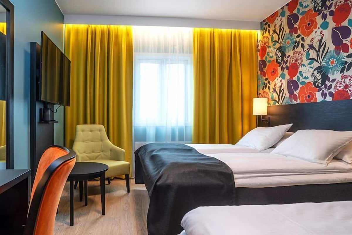 A hotel room with a bed, a desk, a chair, a TV, and a window with curtains.