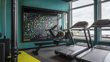 Un gimnasio con cintas de correr, una banca de pesas y un llamativo mural.