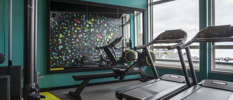 Un gimnasio con cintas de correr, una banca de pesas y un llamativo mural.