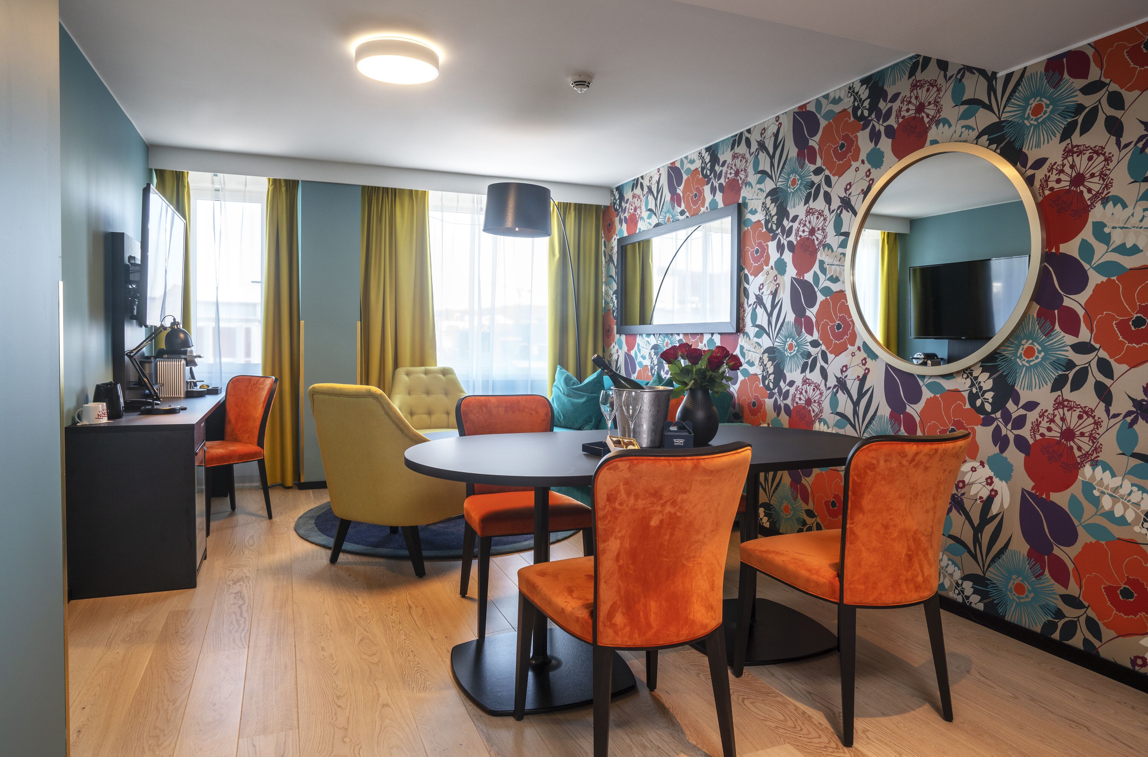 A dining area with a round table, orange chairs, a black desk, and a TV.
