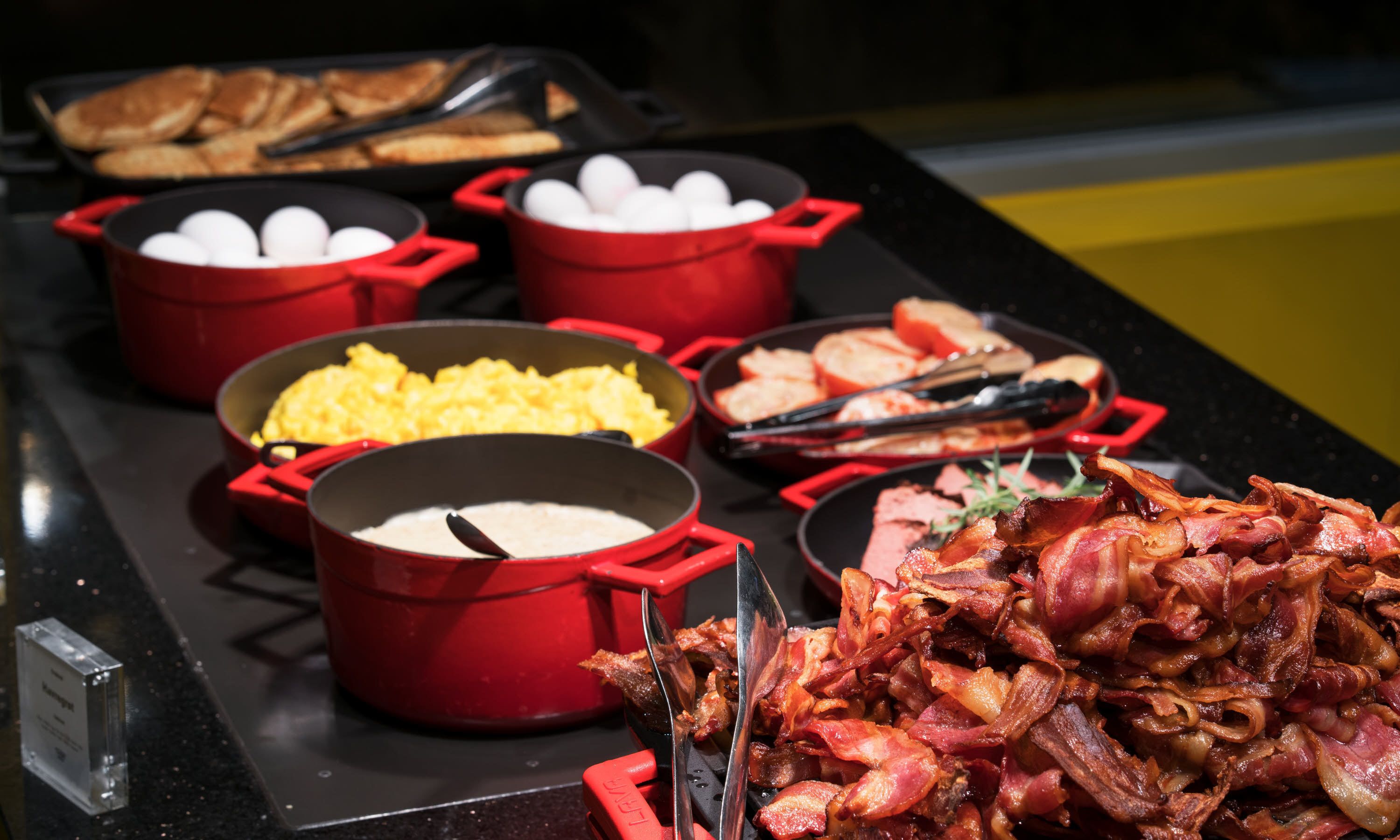 Un bufé con diversas opciones de comida, incluyendo huevos, huevos revueltos, tocino y salchichas.