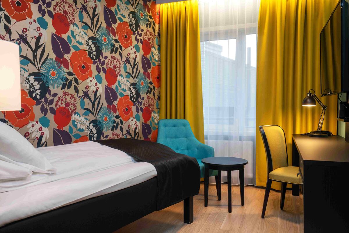 A hotel room with a bed, a desk, a chair, and a small table.