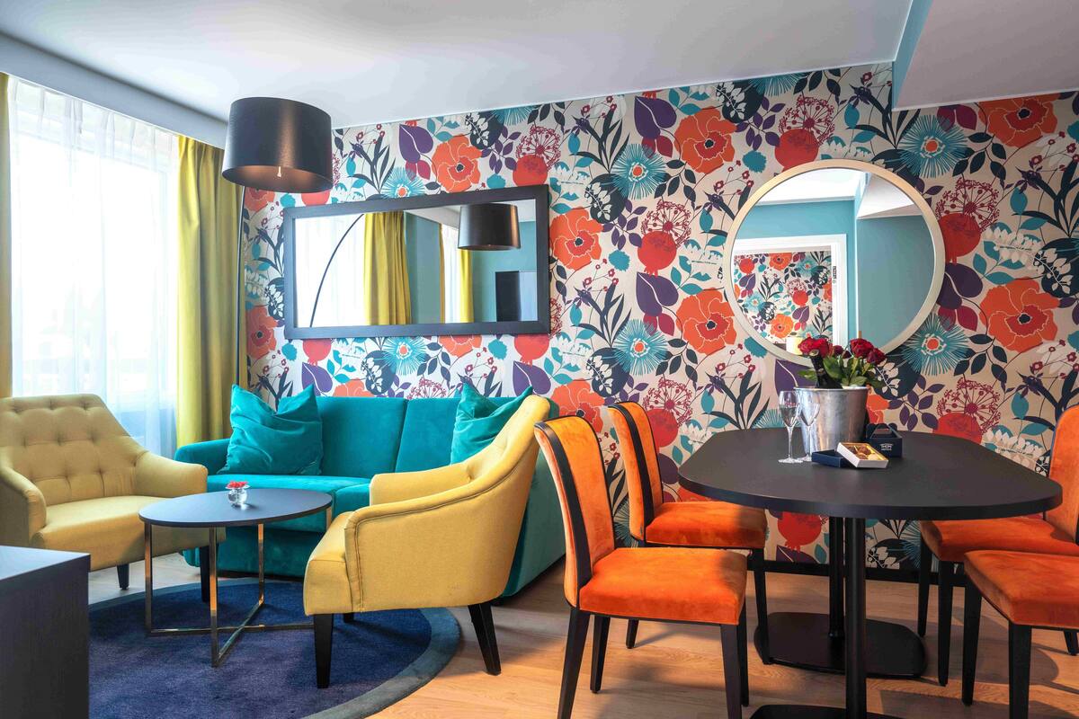 A room with a sofa, armchairs, a round table, and a mirror.