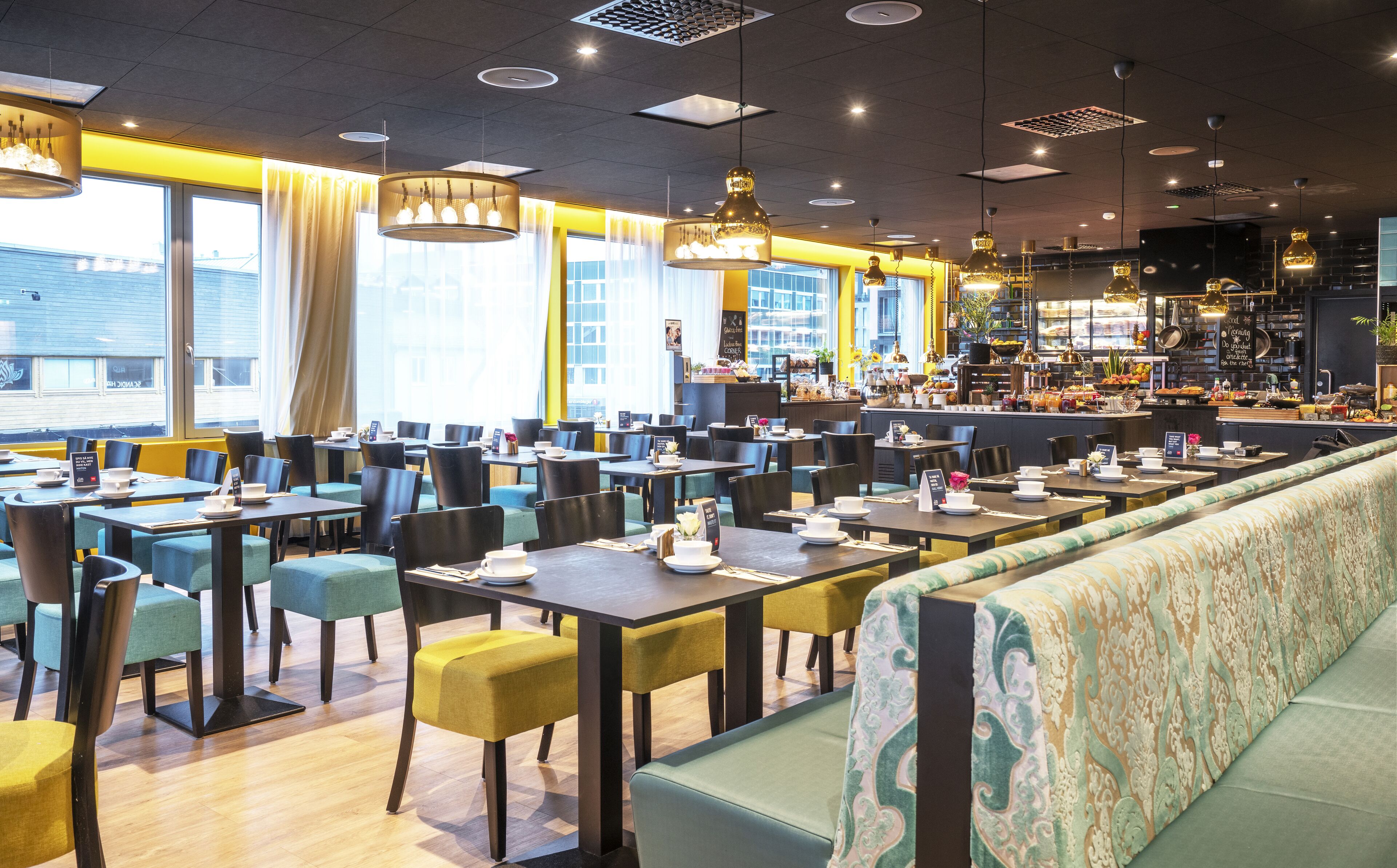 Un restaurante moderno con varias mesas y sillas, una zona de bar y ventanas amplias que dejan entrar luz natural.