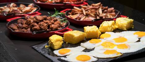 A breakfast buffet with various dishes including scrambled eggs, fried eggs, and different types of meat and vegetables.
