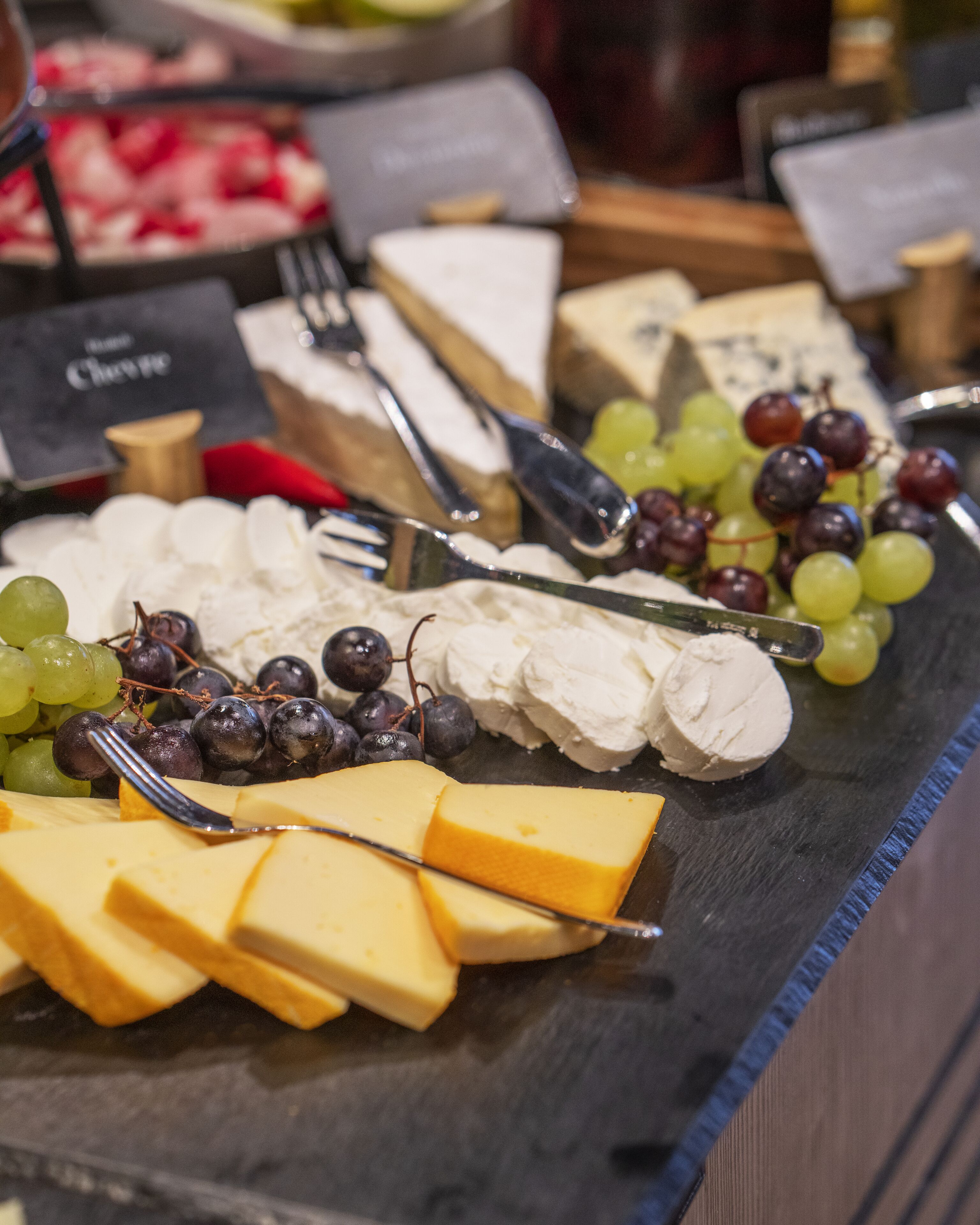 A cheese board with various cheeses, grapes, and a knife.
