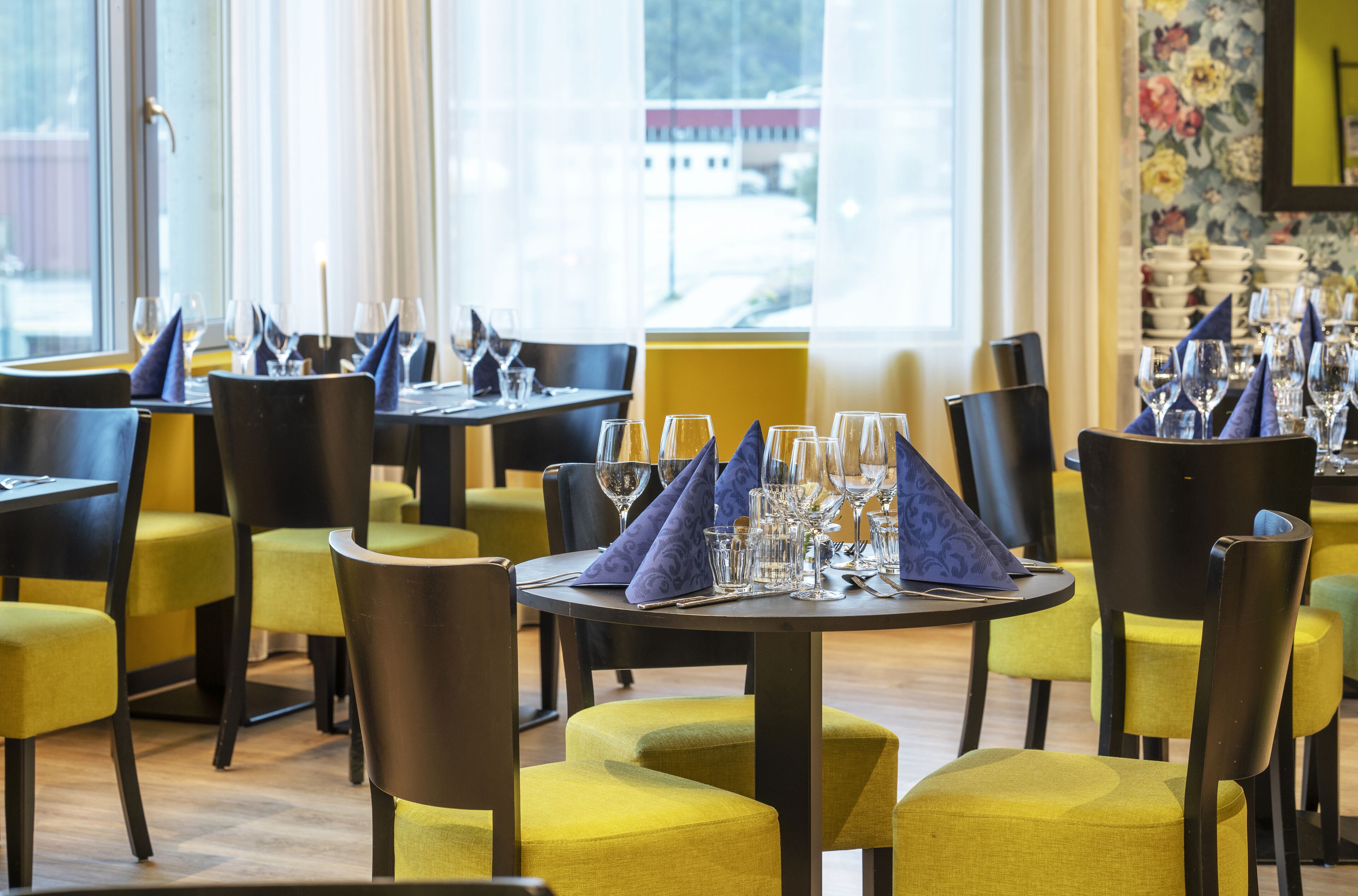 A restaurant interior with round tables, yellow chairs, and a view of a building outside.