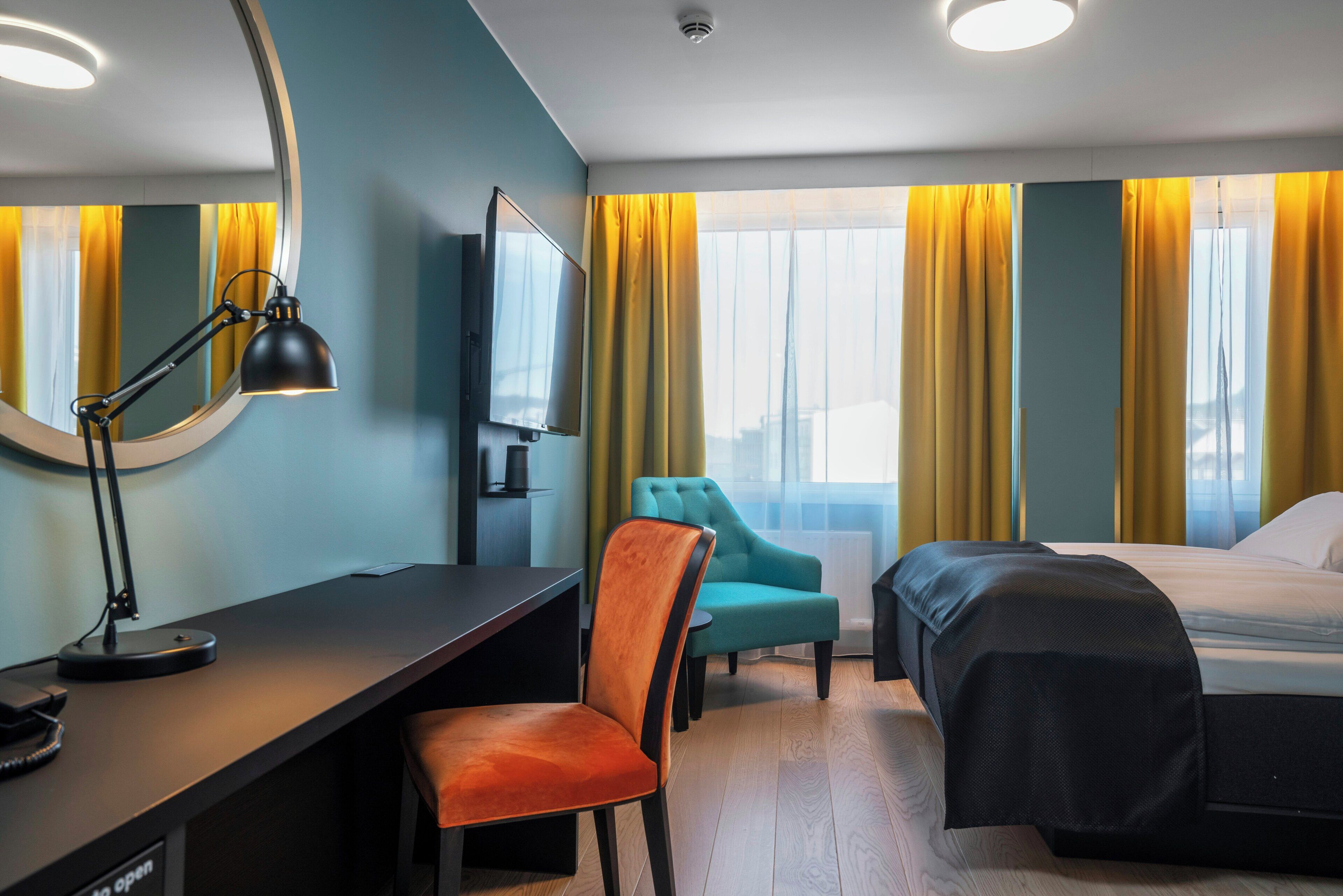 A hotel room with a desk, a chair, a bed, and a television.