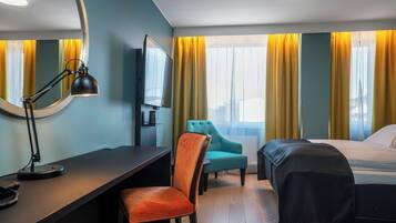 A hotel room with a desk, a chair, a bed, and a television.
