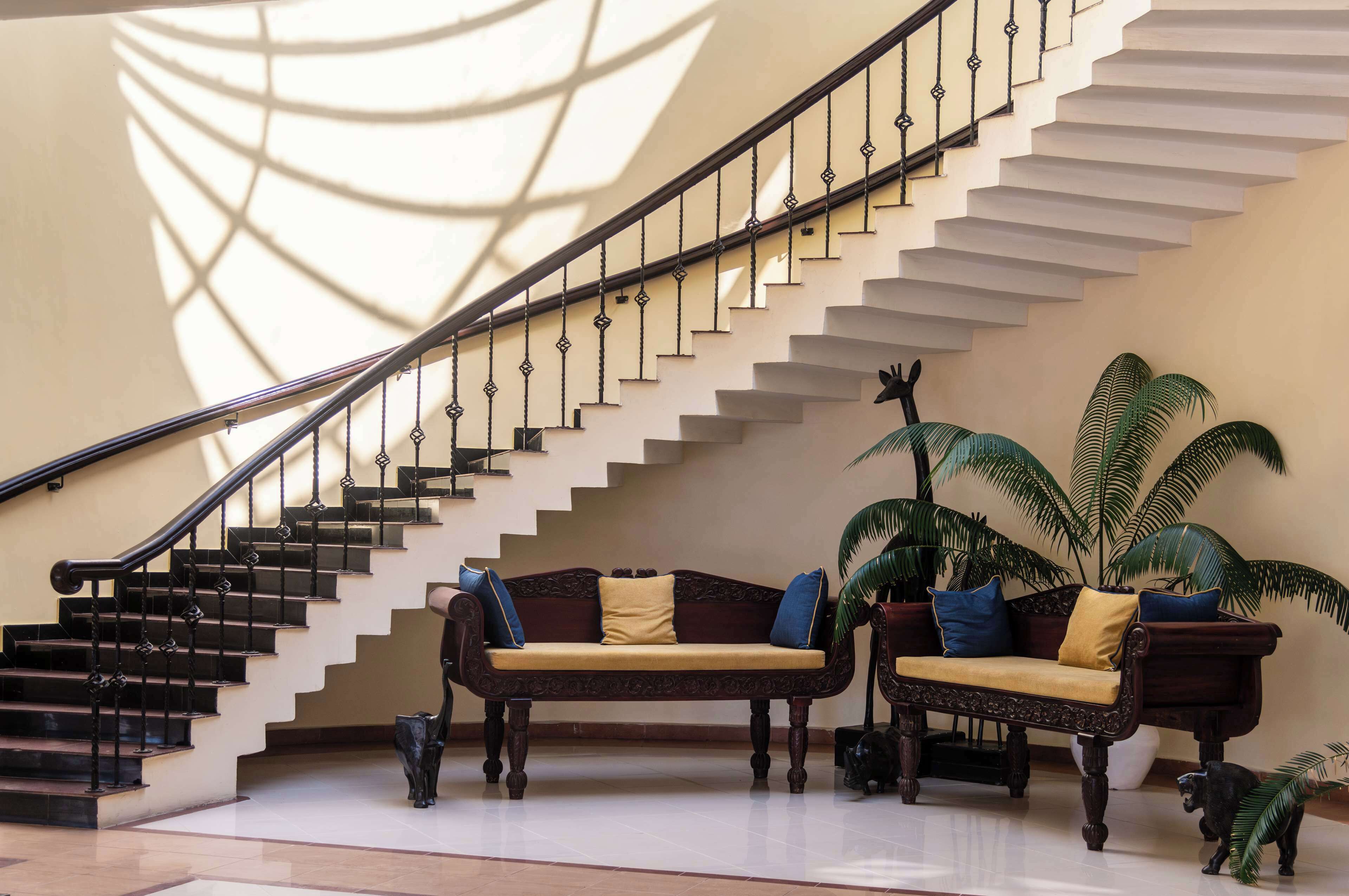 A grand staircase with ornate railings, a plush sofa with cushions, and a large potted plant.