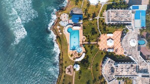 Eine Luftaufnahme eines Resorts mit mehreren Schwimmbecken, einem großen zentralen Pool und einem Strandbereich.