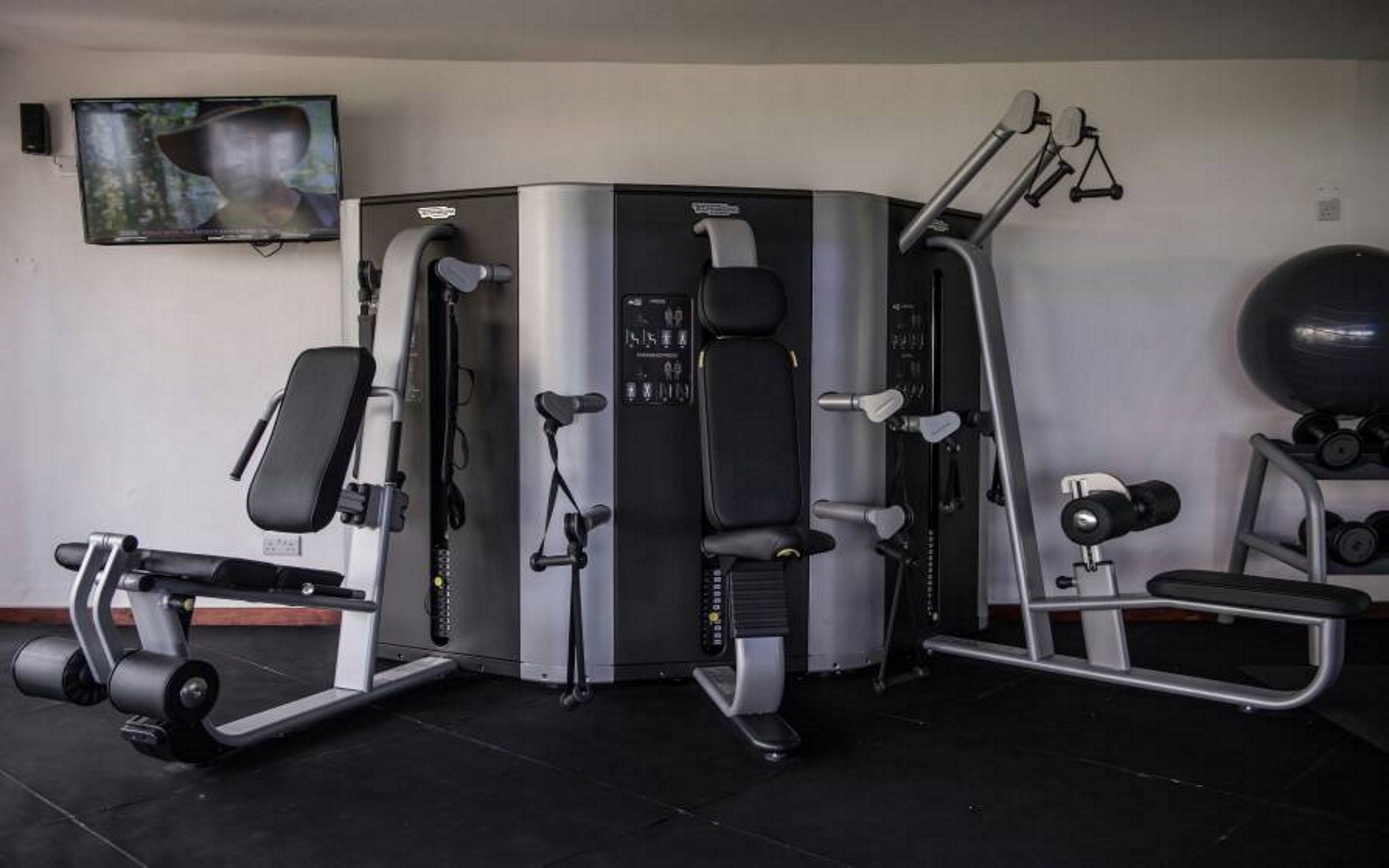 A gym with a variety of exercise equipment including a leg press machine, a bench press, and a cable machine.