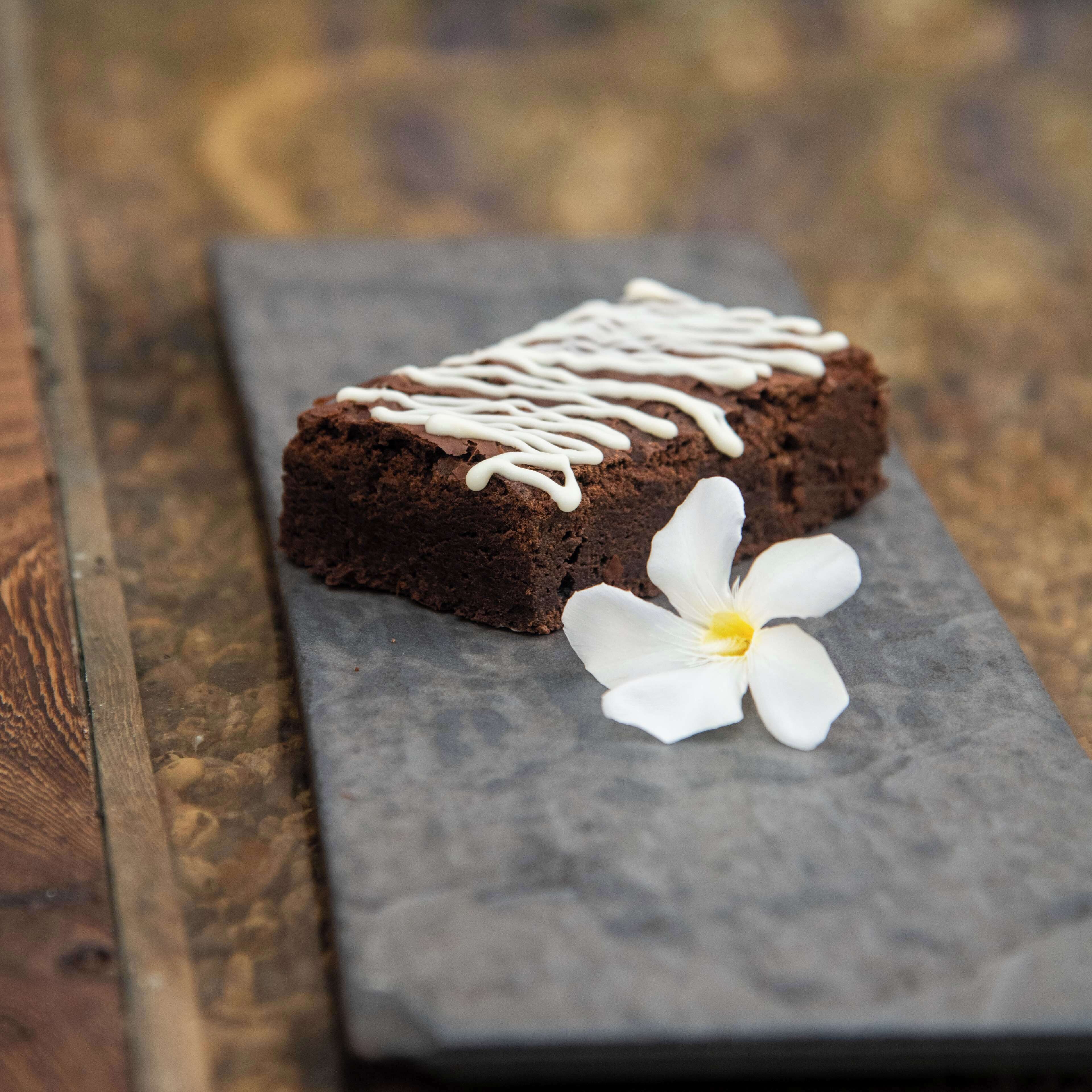 Un brownie solo sobre una tabla de pizarra, con una flor blanca a su lado.