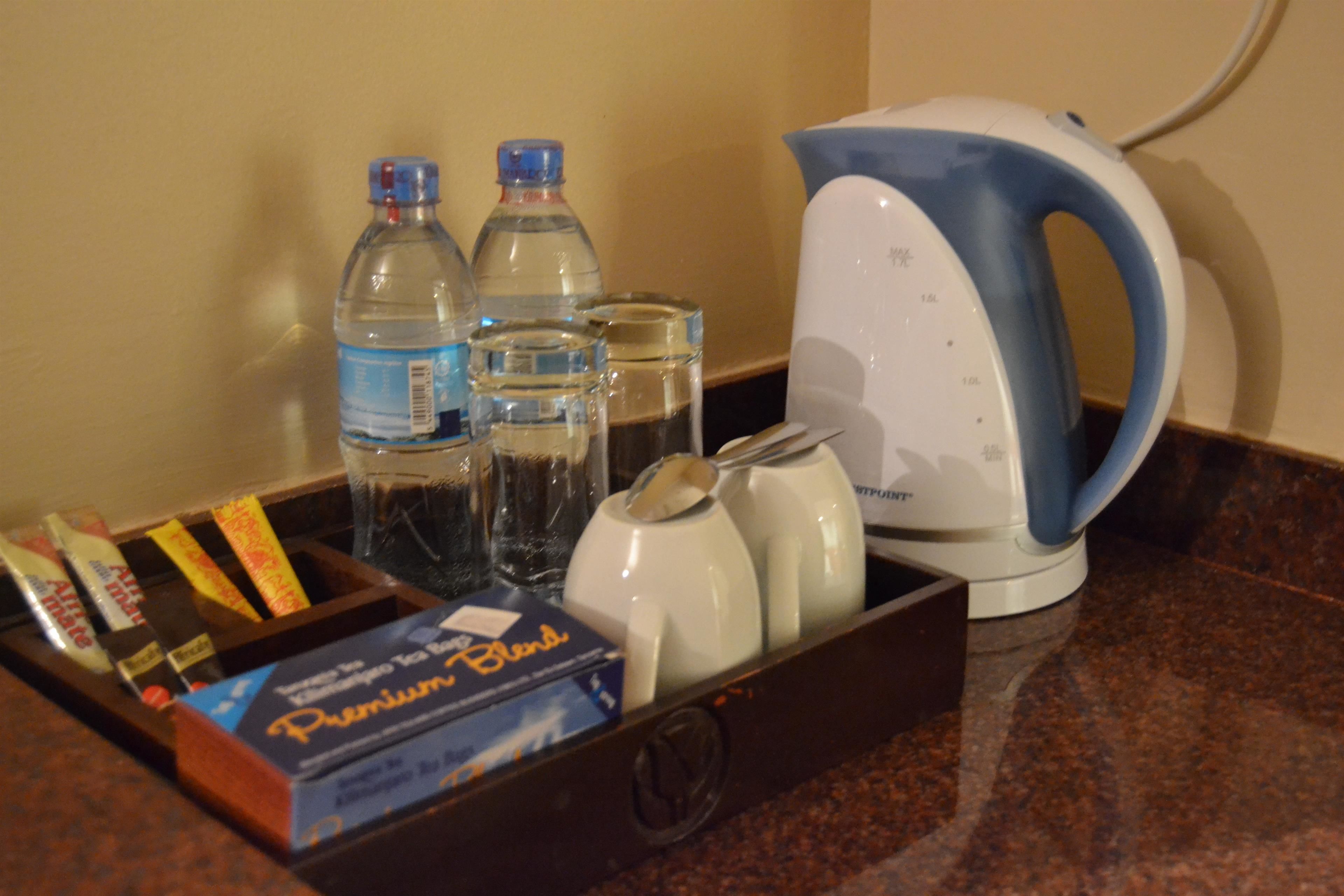 Un plateau contenant une boîte de café en grains de qualité supérieure, deux bouteilles d’eau et une bouilloire électrique blanche, le tout posé sur un plan de travail en granit.