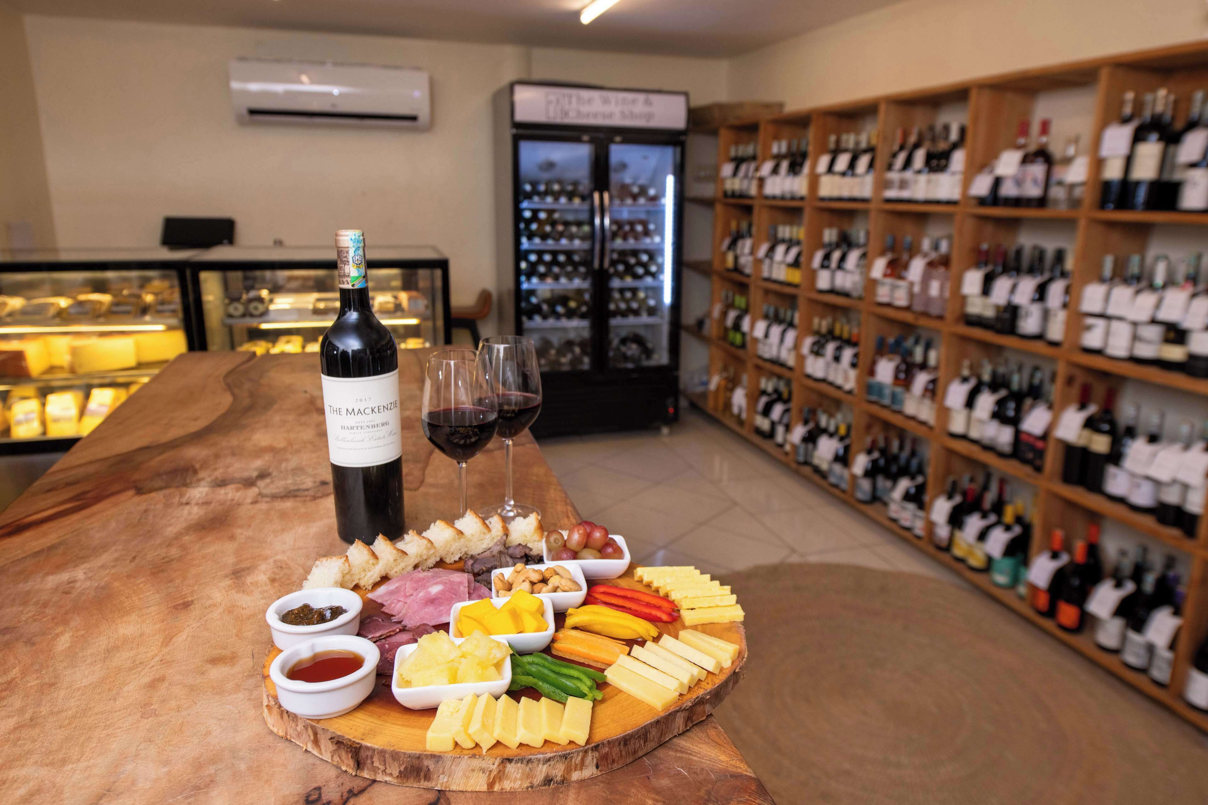 A wine tasting setup with a wooden table displaying various cheeses, meats, and fruits. A bottle of wine and glasses are also present.