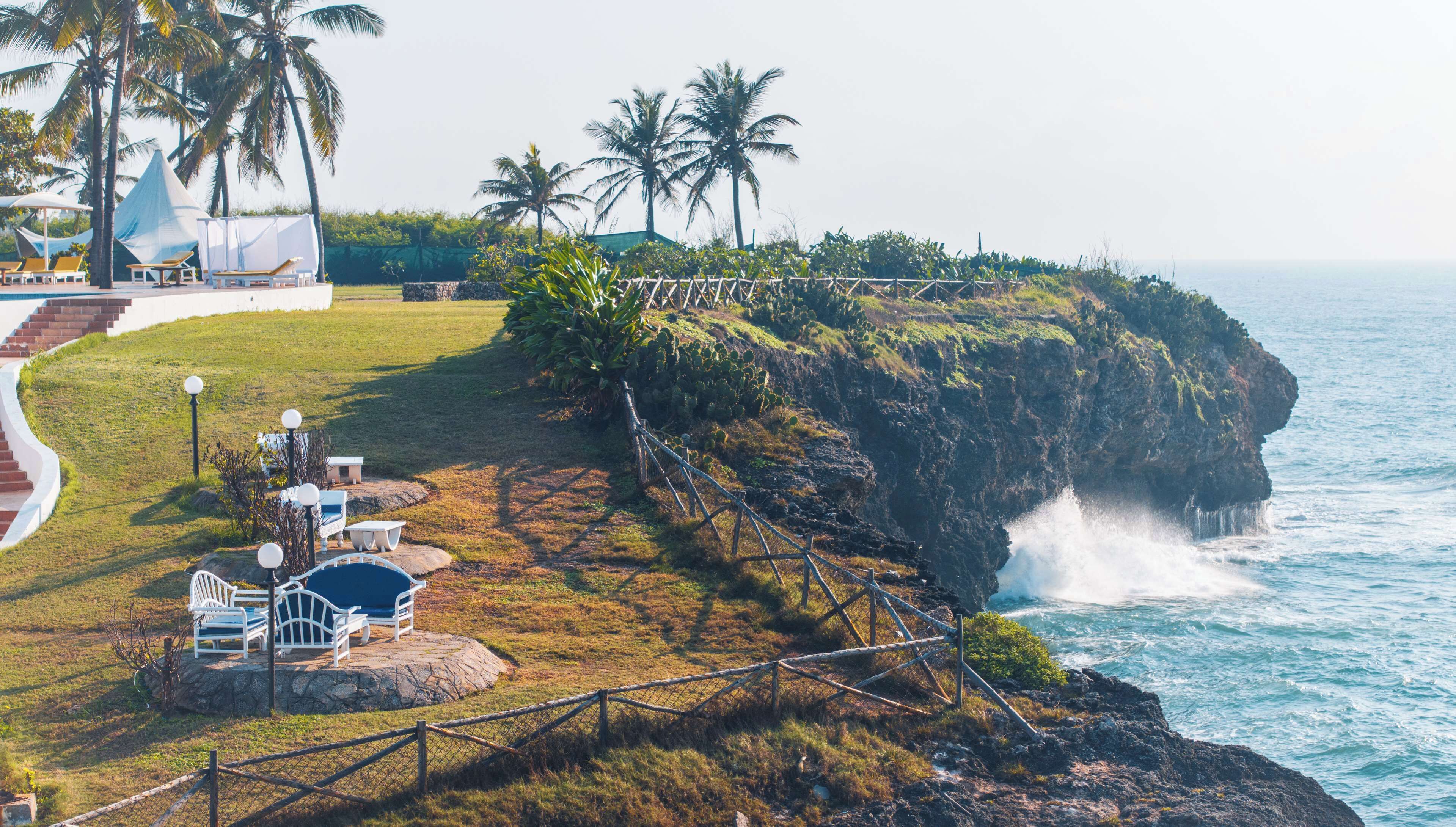 A coastal area with a seating area, palm trees, and a view of the ocean.