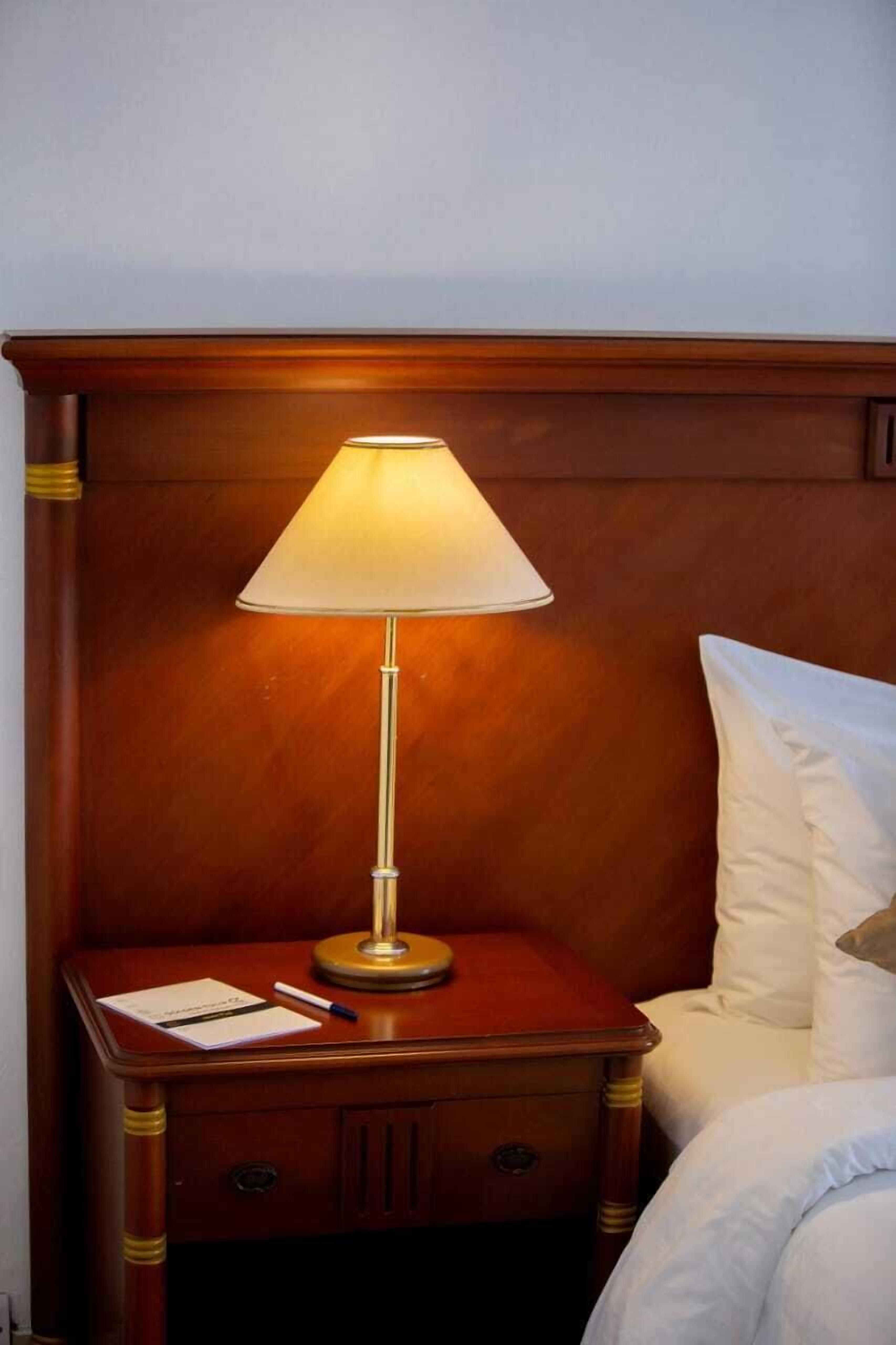 A wooden bedside table with a lamp, a notepad, and a pen.