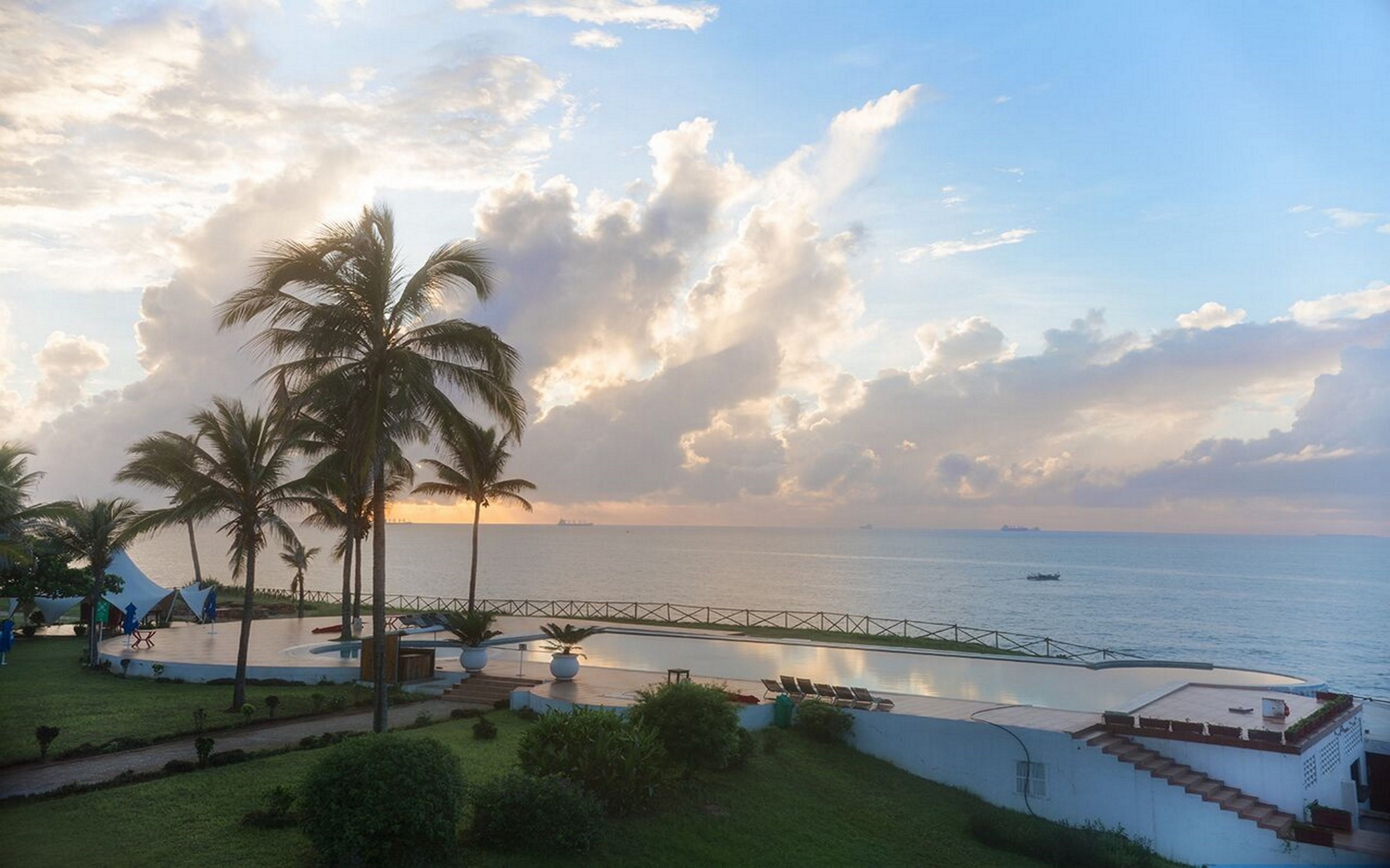 Un resort costero con palmeras, piscina y vistas al mar.