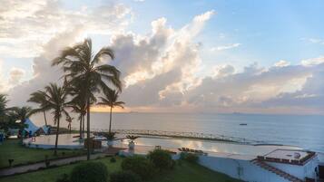 Un resort costero con palmeras, piscina y vistas al mar.