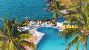 A resort with a large swimming pool, palm trees, and a view of the ocean.