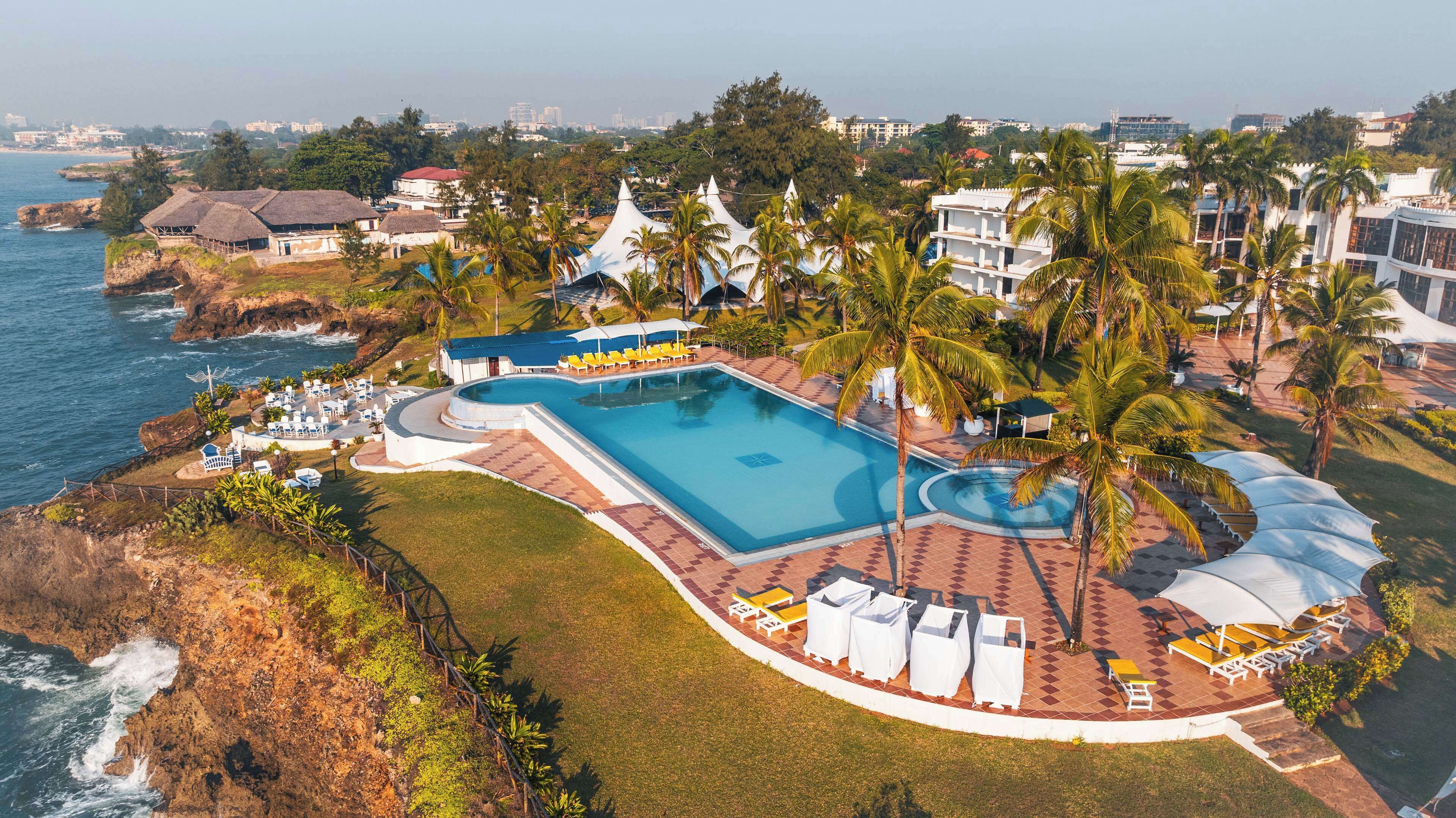 Un resort con una piscina grande, palmeras y vistas al océano.