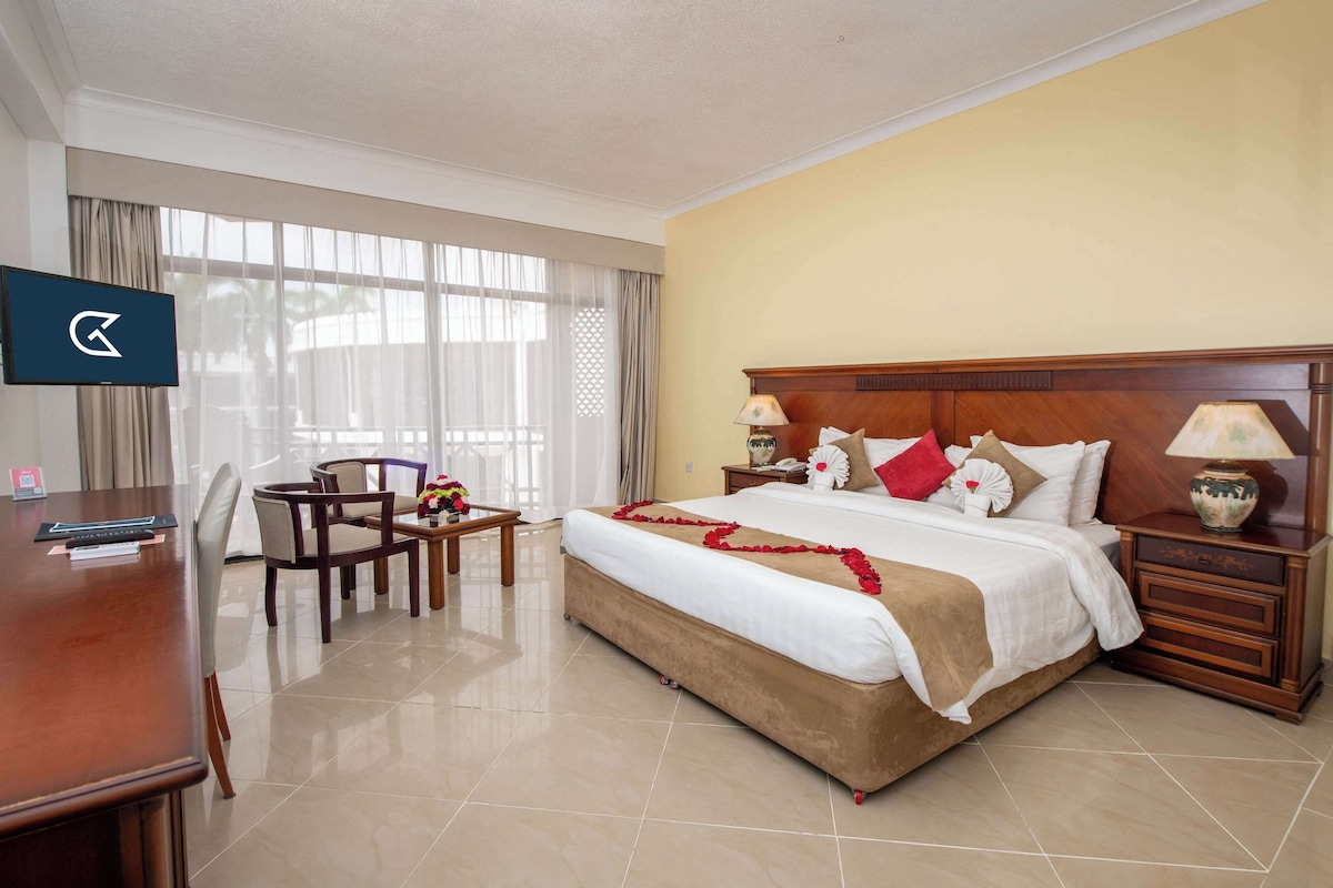 Habitación de hotel con una cama grande, un escritorio, una silla, un televisor y una ventana con cortinas.