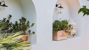 Un muro bianco con due finestre ad arco, ciascuna con una pianta in vaso e un punto luce a parete.