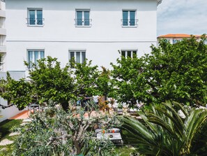 A white building with balconies, surrounded by lush green trees and plants. - La Villa Cannes Croisette (Cannes)