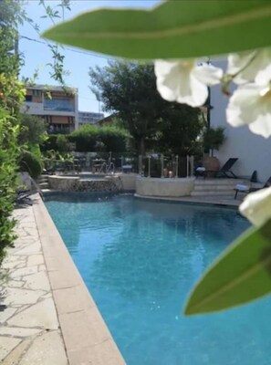 A swimming pool with a stone border, surrounded by greenery and a few lounge chairs. - La Villa Cannes Croisette (Cannes)