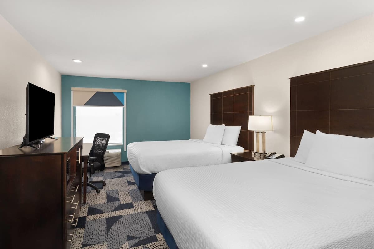 Quarto de hotel com duas camas, uma mesa de trabalho com televisão, uma cadeira e uma janela com vista.