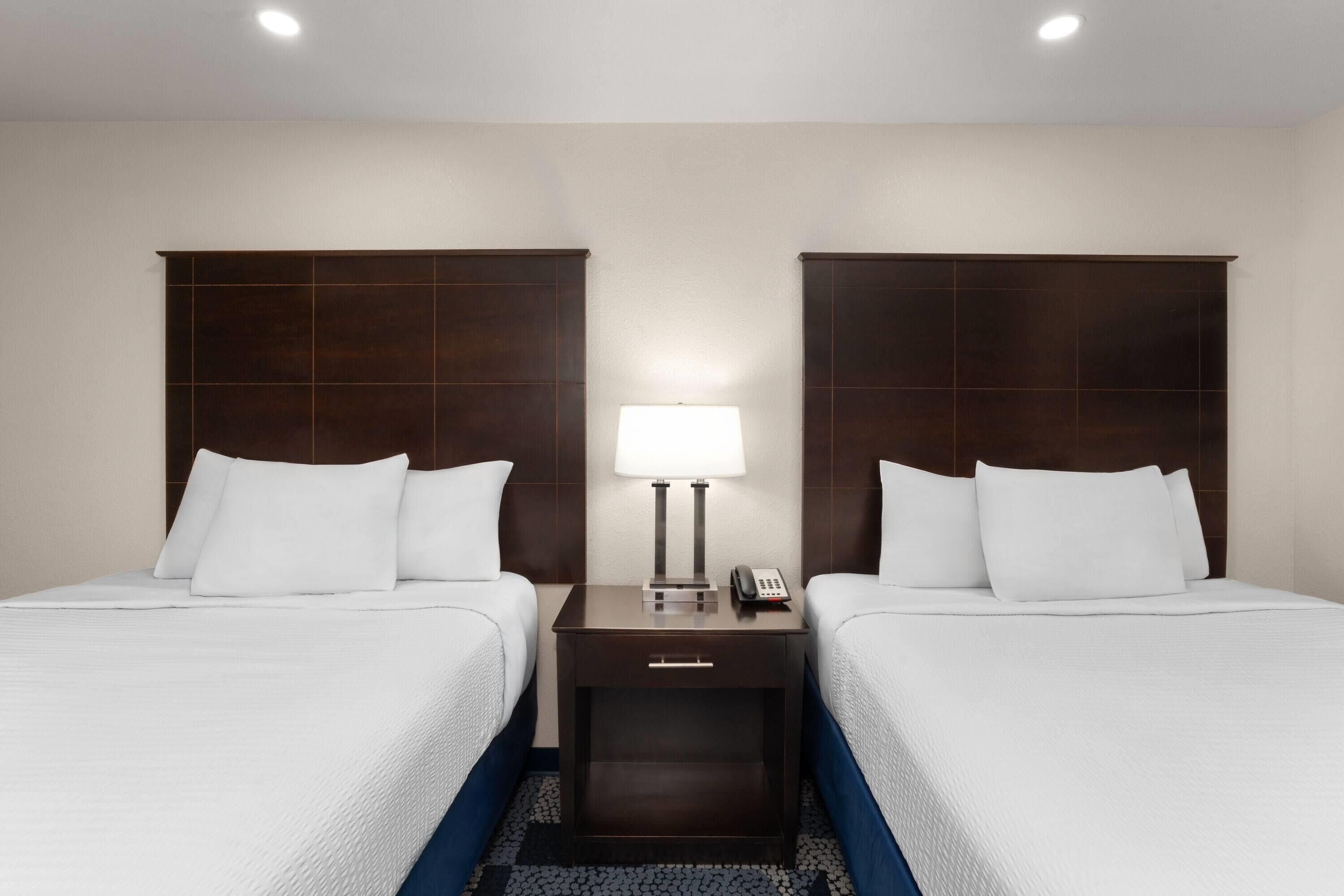 A hotel room with two beds, a nightstand with a lamp, and a phone.