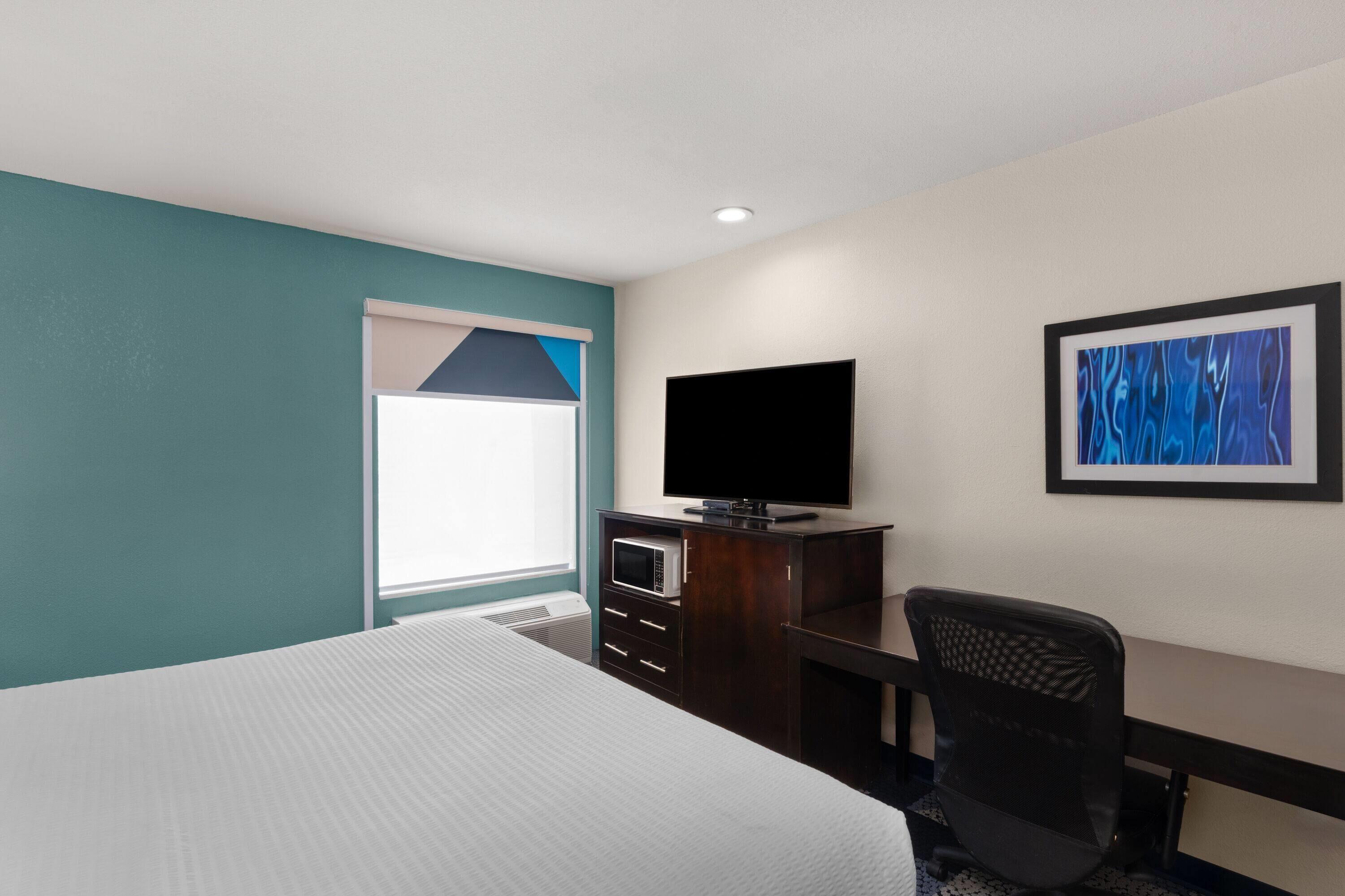 Una habitación de hotel con una cama, un escritorio, un televisor y un cuadro en la pared.