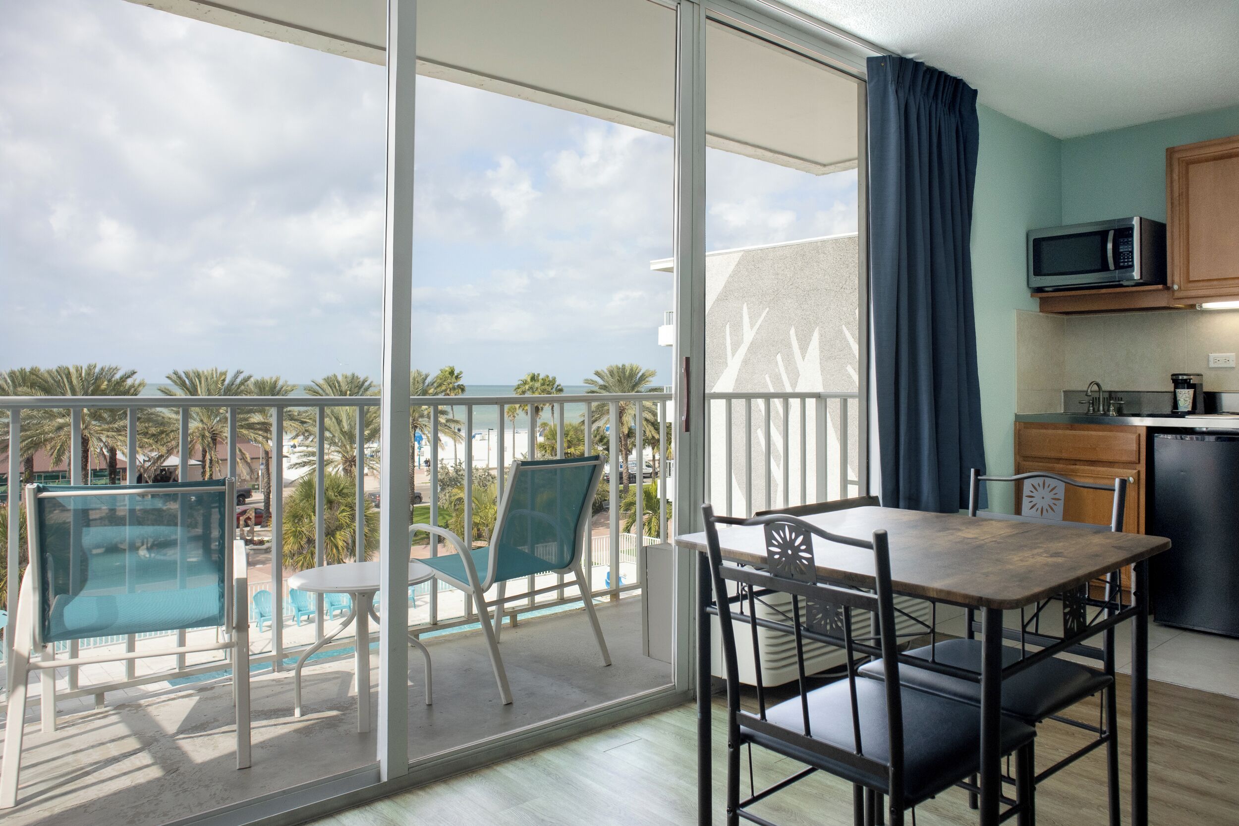 A balcony with a pool, a dining table with chairs, and a kitchen area with a microwave.