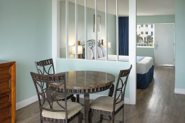 A dining area with a round table and four chairs, a wooden dresser, and a bed in the background. - The Beachview Inn Clearwater Beach (Clearwater Beach)