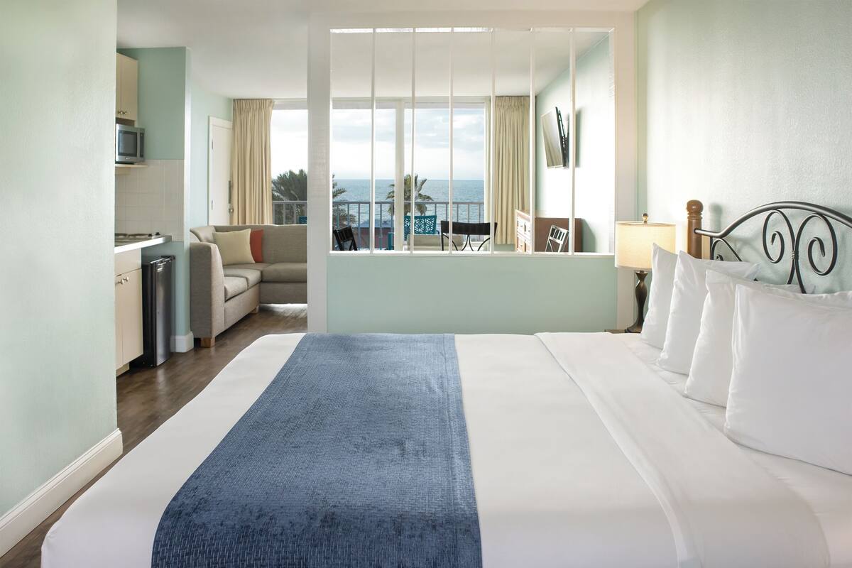 Quarto de hotel com uma cama grande, um sofá, uma mesa de jantar e vista para o mar.