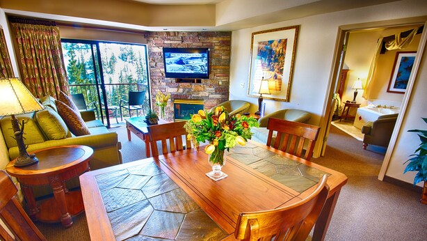A spacious living room with a stone fireplace, a television mounted on the wall, and a dining area with a wooden table and chairs. - Ridge Pointe (Stateline)