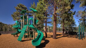 A playground with multiple slides and climbing structures, surrounded by trees and a clear sky. - Ridge Pointe (Stateline)